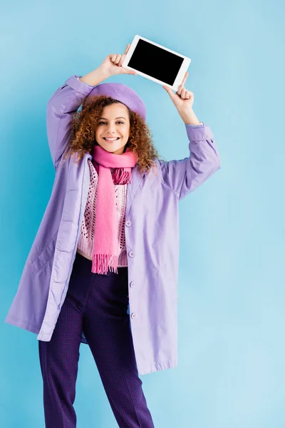 幸せな若い女性です冬のコート ベレー帽とピンクのニットスカーフ保持デジタルタブレット上の頭の上にブルー — ストック写真