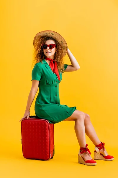 全身上下都是笑容满面的女人 戴着草帽 戴着太阳镜 穿着衣服 坐在黄色的行李上 — 图库照片