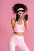 starke junge Frau in Sportbekleidung mit Fesseln an den Händen isoliert auf rosa
