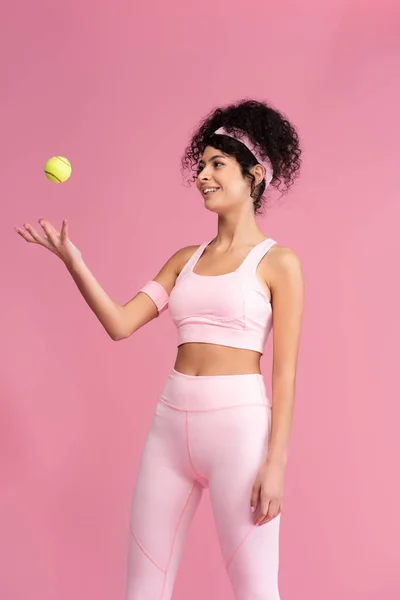 ピンク色に隔離された空気中にテニスボールを投げる幸せとスポーツ女性 — ストック写真