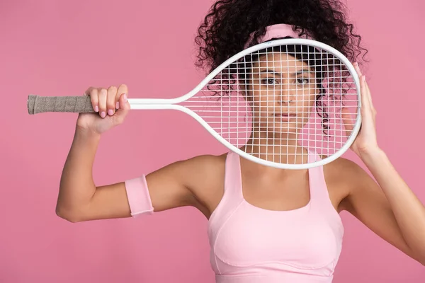 年轻而活泼的女子通过用粉色隔开的网球拍看着镜头 — 图库照片