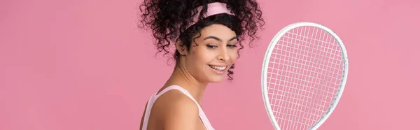 happy and sportive woman holding tennis racket isolated on pink, banner