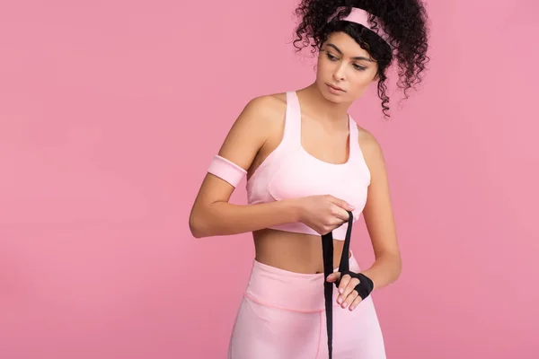 curly woman in sportswear wrapping hand with bondage isolated on pink
