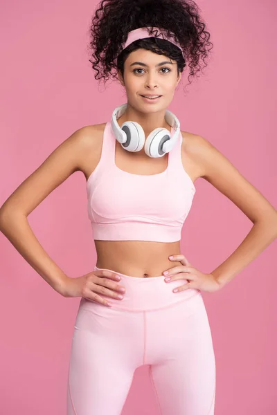 Krullende Jonge Vrouw Draadloze Hoofdtelefoon Staan Met Handen Heupen Geïsoleerd — Stockfoto