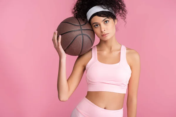 ピンク色に隔離されたカメラを見ながらバスケットボールをしている巻き若い女性 — ストック写真