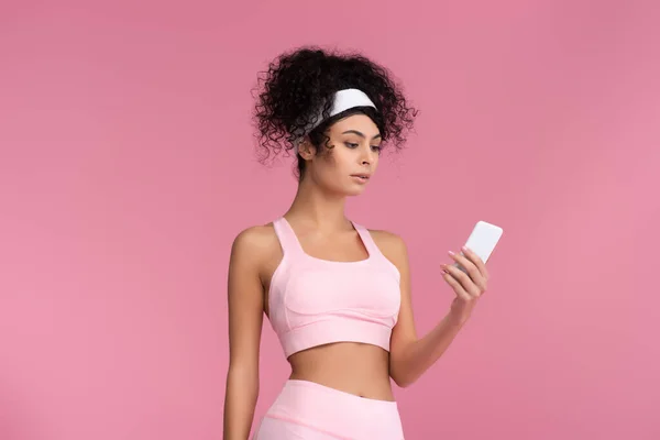 Krullende Jonge Sportvrouw Met Behulp Van Smartphone Geïsoleerd Roze — Stockfoto