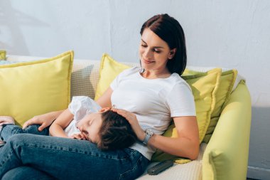 Gülümseyen anne kanepede uyuyan kızına bakıyor.