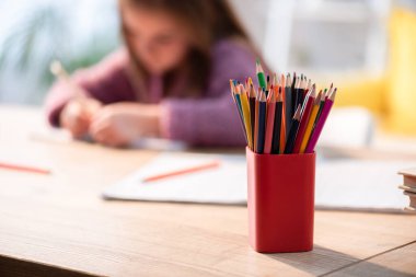 Masanın üzerinde renkli kalemler ve arka planda bulanık bir kız.