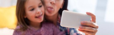 Mother and daughter with sticking out tongues taking selfie on blurred background, banner clipart