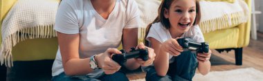 KYIV, UKRAINE - 19 Ekim 2020: Mutlu kız, evde annesinin yanında joystick ile oynuyor, pankart