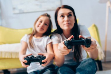 KYIV, UKRAINE - 19 Ekim 2020: Bulanık arka planda evde joysticklerle oynayan pozitif anne ve kız