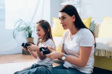 KYIV, UKRAINE - 19 Ekim 2020: Gülümseyen anne ve kız, bulanık arka planda yerde joysticklerle oynarken gözlerini kaçırıyorlar