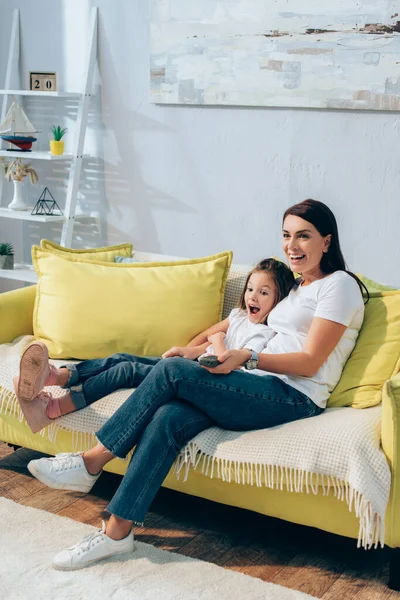 Full Length Happy Mother Remote Controller Hugging Excited Daughter Couch — Stock Photo, Image