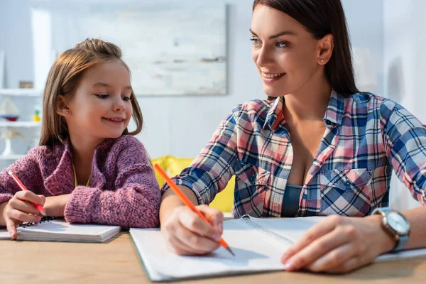 Lächelnde Mutter Blickt Tochter Während Sie Schreibtisch Auf Verschwommenem Hintergrund — Stockfoto