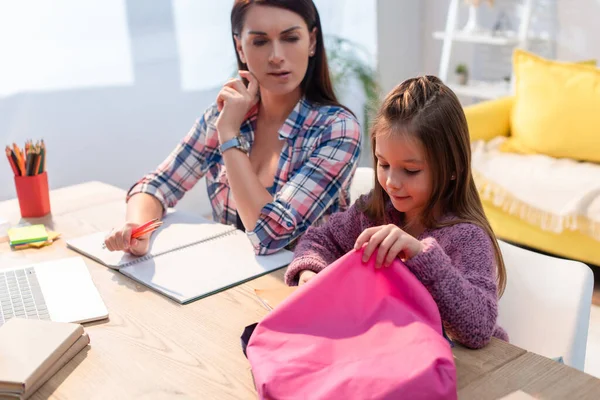 Positive Tochter Mit Rucksack Sitzt Neben Seriöser Mutter Schreibtisch Auf — Stockfoto