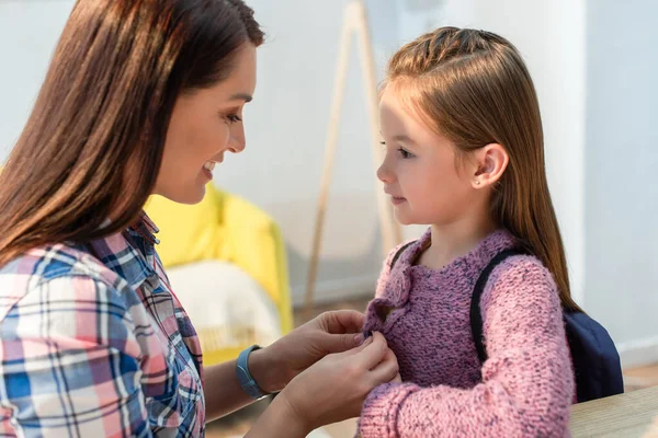 Glimlachende Moeder Krijgen Aangekleed Dochter Met Rugzak Thuis Wazig Achtergrond — Stockfoto