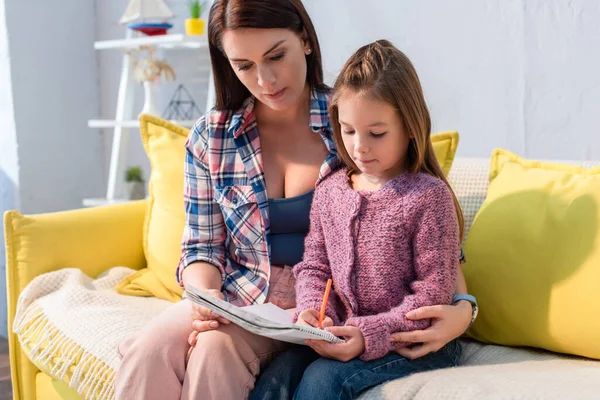 Mãe Abraçando Filha Escrevendo Livro Cópia Sofá Fundo Embaçado — Fotografia de Stock