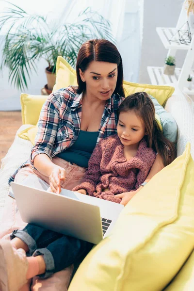 Madre Parlando Guardando Computer Portatile Mentre Abbraccia Figlia Sul Divano — Foto Stock