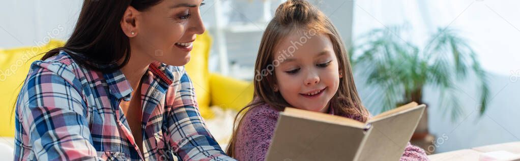 Positive mother and daughter reading book at home on blurred background, banner