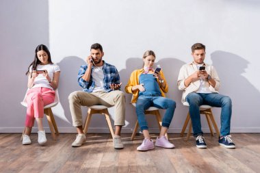 Çok ırklı insanlar koridorda beklerken sandalyede akıllı telefon kullanıyorlar. 