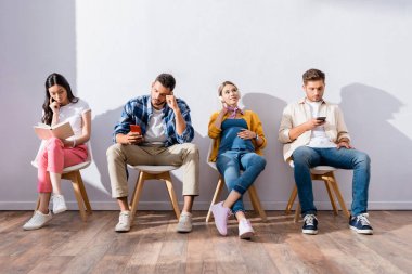 Çok ırklı insanlar akıllı telefonlar kullanıyor ve salondaki sandalyeler üzerine kitap okuyor. 