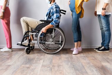 Disabled man in medical mask sitting in wheelchair near pregnant woman in queue  clipart
