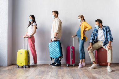 Tıbbi maskeli çok ırklı insanlar havaalanında bavullarıyla bekliyor. 