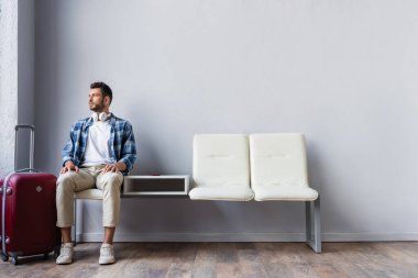 Havaalanında bagajın yanında oturan kulaklıklı genç adam. 