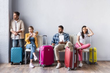 Stresli çok kültürlü insanlar havaalanı koridorundaki bavulların yanından uzağa bakıyor. 
