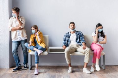 Tıbbi maskeli şüpheci çok ırklı insanlar kuyruktaki sandalyedeki adama yan gözle bakıyor. 