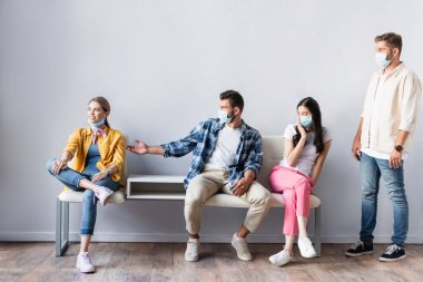 Tıbbi maskeli kuşkucu çok kültürlü insanlar kuyruktaki gülümseyen kadını işaret ediyor. 