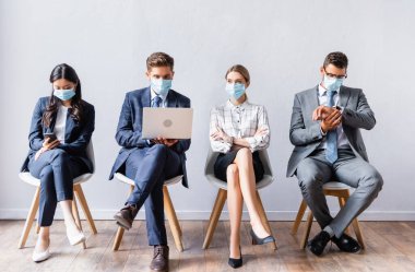 İş görüşmesinden önce tıbbi maskeli çok ırklı iş adamları cihaz kullanıyor. 