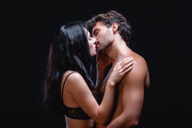 Baştan çıkarıcı esmer bir kadının, siyahlar içinde yalnız ve seksi üstsüz bir adamı öpmesinin yan görünüşü.