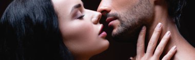 side view of sexy brunette woman kissing young man isolated on black, banner clipart