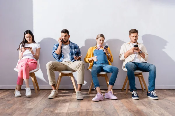 Pessoas Multiétnicas Usando Smartphones Cadeiras Enquanto Esperam Salão — Fotografia de Stock