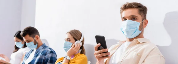 Homem Máscara Médica Com Smartphone Olhando Para Câmera Perto Pessoas — Fotografia de Stock