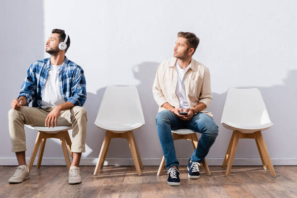 Мужчины со смартфоном и наушниками смотрят в сторону, сидя в холле 