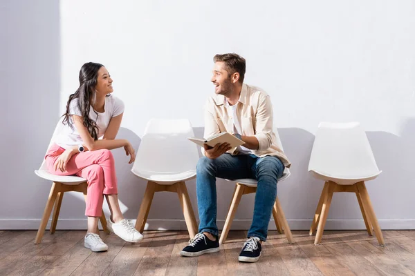 Smiling Man Book Taking Asian Woman Queue Chairs — Stock Photo, Image