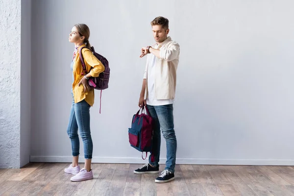 Estudiante Verificando Tiempo Reloj Pulsera Cerca Mujer Con Mochila Pasillo — Foto de Stock