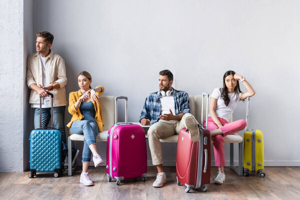 Stressed multicultural people looking away near suitcases in hall of airport 