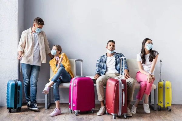 Multicultural people in medical masks waiting near suitcases in airport