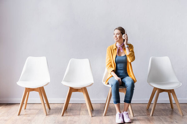 Веселая женщина в наушниках, сидя на стуле в холле 