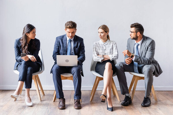 Multiethnic businesspeople looking at businessman with laptop before job interview in office 