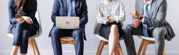 Обрезанный вид бизнесменов с ноутбуком и смартфоном, сидящих на стульях в офисе, баннер 