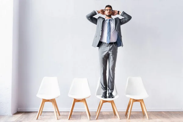 Businessman standing on chair near wall in office
