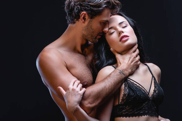 Мужчина без рубашки обнимает шею сексуальной женщины в кружевном лифчике, изолированном от черного