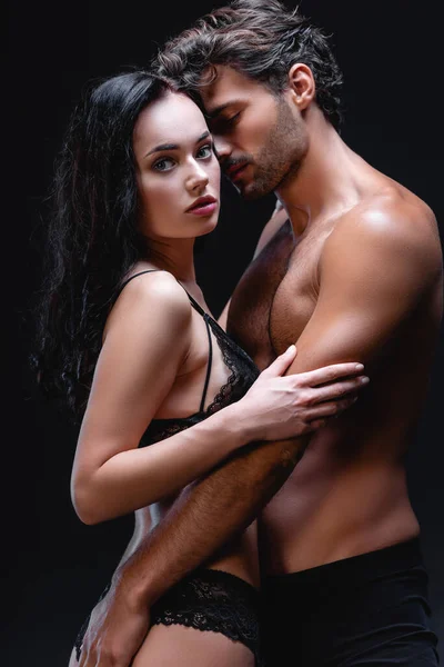 Seksi üstsüz adam, seksi esmer kadına sarılıyor ve siyah kameraya bakıyor.