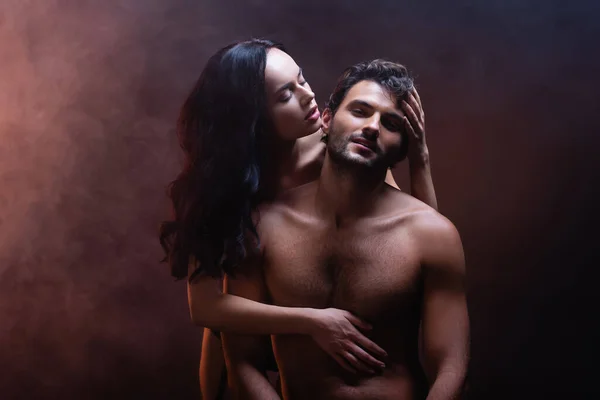 性感女人在黑漆漆的背景下抱着赤身裸体的肌肉男人 — 图库照片