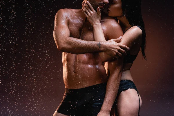 在雨滴下 性感女人在黑暗背景下搂着赤裸的肌肉男人脖子的剪影 — 图库照片