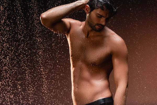 stock image shirtless man with muscular torso posing with hand on head under rain on dark background